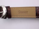 Close-up of the brown leather strap's underside, embossed with 'Stauer' and 'Genuine Leather'.