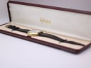 The Bulova watch resting inside an open rectangular burgundy presentation box with "SHIMA" written in gold on the lining.