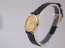 Angled view of the Raymond Weil 9920 watch, showing the slender gold case and black strap on a watch stand.