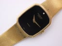 Close-up front view of Raymond Weil watch with gold tonneau case, black dial, gold hands, and single diamond marker.