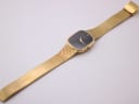 Full view of the Raymond Weil watch, laid flat, showing the long gold mesh bracelet and tonneau case.