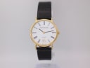 Front view of Mappin & Webb quartz watch with gold case, white dial, black Roman numerals, and black lizard-effect leather strap on a clear stand.