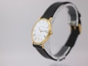 Angled side view of Mappin & Webb watch showing the gold-plated case, crown, and black leather strap on a clear stand.