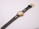 Top-down view of the Michel Jordi watch with its green embroidered leather strap laid flat, showcasing the full length of the decorated strap.