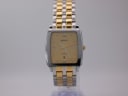 Front view of the Rado Diastar watch with gold dial and two-tone bracelet, presented on a clear stand.