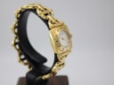 Angled left-side view of the gold-tone Gucci 6400 L watch on a display stand, showing the curved profile of the bracelet.