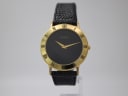 Front view of the Gucci 3000.2.M watch, showing its black dial, gold tone case, and black textured leather strap.