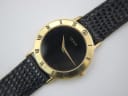 Close-up of the Gucci 3000.2.M watch dial, showing the minimalist black face, gold hands, and 'GUCCI' logo at 12 o'clock.