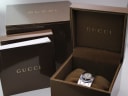 The original Gucci branded brown presentation box and a booklet, with the watch nestled inside, against a white background.