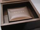 Inside view of the Gucci branded brown box, revealing a compartment and the padded watch cushion.