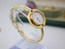 Another angled side view of the Gucci 1100-L watch on a clear display stand, showing the simple, uncluttered white dial.