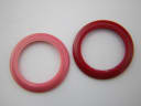 Close-up top-down view of two interchangeable bezels, one pink and one red, against a white background.