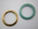 Close-up top-down view of a plain gold-tone bezel and a teal interchangeable bezel, against a white background.