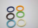 Top-down view of six assorted coloured interchangeable bezels laid out on a white surface.