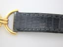 Close-up of the black leather strap, showing its lizard-effect texture and stitching near the integrated gold-tone link.
