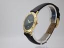 Left angled view of the gold-tone Gucci 3000 M watch on a clear stand, highlighting the Roman numeral bezel and case profile.