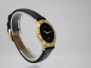 Right angled view of the gold-tone Gucci 3000 M watch on a clear stand, showing the signed crown and strap texture.