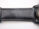 Detailed view of the black leather strap with its embossed Gucci 'G' monogram pattern.