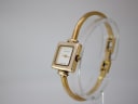 Angled side view of the Gucci 1900 L watch on a clear stand, highlighting the integrated gold-tone bangle bracelet.