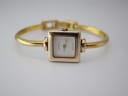 Front view of the Gucci 1900 L watch on a white surface, showcasing the gold-tone square case and white dial with "GUCCI" branding.