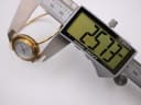 A digital caliper measuring the case diameter of the Gucci watch, displaying a precise reading of 25.37mm.