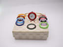 The Gucci watch with a red bezel, surrounded by a selection of other colourful interchangeable bezels, sitting on its original Gucci box.