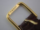 Close-up of the gold tone Tissot-signed buckle on the brown leather strap.