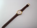 Full view of the Tissot watch laid flat, showing the brown leather strap and gold tone case.