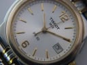 Extreme close-up of the Tissot PR 50 watch dial, showing the white texture, gold baton and Arabic indices, date window, and "SWISS MADE I" text.