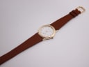 Top down view of the Mappin & Webb watch with its brown leather strap and gold tone buckle.