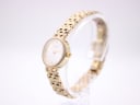Angled side view of the Tissot T058009 A watch on a clear stand, highlighting the gold tone case and bracelet.