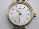 Close-up of the Tissot T058009 A watch dial, showing the silver sunburst finish, applied gold baton indices, "TISSOT 1853" and "SWISS MADE" text.