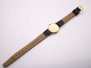 View of the watch from the back, showing the case back and the underside of the black leather strap