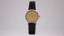Front view of the Tissot C226K watch showing the champagne dial, gold-tone baton indices, and two-tone case on a dark brown textured leather strap.