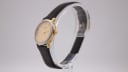 Side profile of the Tissot C226K watch, showcasing the two-tone case, gold-tone crown, and dark brown leather strap on a display stand.