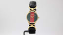 Front view of the Gucci 6000.2.L watch on a display stand, showing the iconic dial and black leather strap.