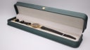 The Gucci 6000L watch laid inside a green leatherette presentation box, showing the watch and strap against a light interior.