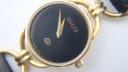 Close-up of the Gucci 6000L black dial, showing gold Gucci logo, interlocking G emblem, 'Swiss Made' text, and gold-tone dauphine hands.