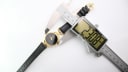 Overhead view of the Gucci 6000L watch being measured by a digital caliper, displaying a case diameter of 23.08mm.