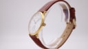 Side profile view of the gold-plated Mappin & Webb watch case and brown leather strap on a display stand.
