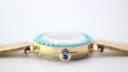 Extreme close-up of the watch crown, featuring a distinctive blue cabochon accent.