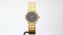 Front view of the gold tone Tissot Stylist watch on a stand, featuring a black dial with diamond markers.
