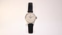 Front view of the vintage Bucherer 109344 ladies watch on a clear display stand, showing the cream dial, silver case, and black leather strap.