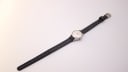 Overhead view of the Bucherer watch with its black leather strap laid flat on a white surface, showing the silver-tone buckle.