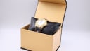 Michel Jordi watch resting on a black cushion inside a light brown presentation box.
