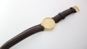 Overhead view of the Tissot watch and full brown leather strap with a gold-tone buckle laid flat.