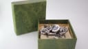 Front view of the Gucci 107 G-Gucci watch inside its original green paisley patterned box, with the lid open.