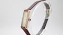 Side profile view of the Raymond Weil 310 watch on a clear stand, highlighting the blue cabochon crown.