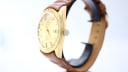 Right side profile view of the gold-tone Royce watch case and crown, with brown leather strap.