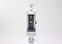 Front view of the Gucci 110 watch, showing the silver-tone rectangular case, black dial with three diamond accents at 12 o'clock, and stainless steel bracelet.